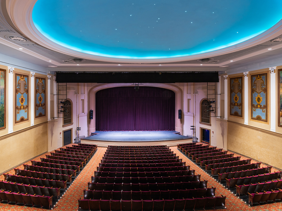 Interior view of the Sottile Theatre showcasing a large stage with a purple curtain and rows of red seats.