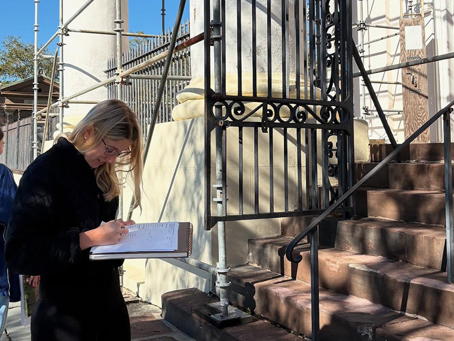 A College of Charleston student take notes in a notepad while observing the architectural details of a historic building.