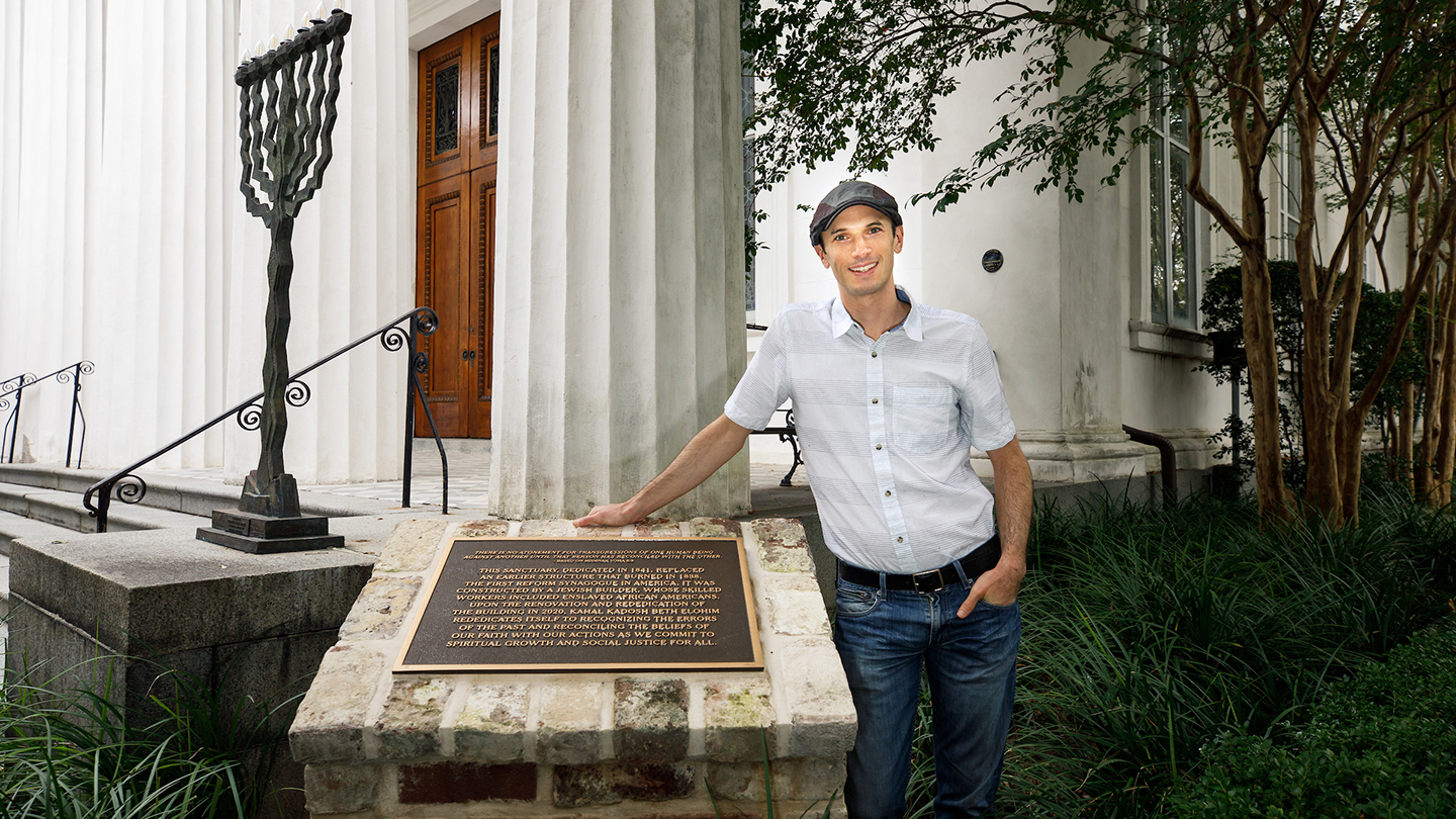 Faculty member standing with dedication plaque at Synagogue