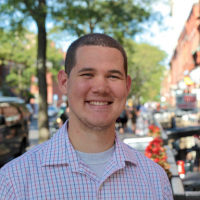 Portrait of Michael Ryan, a man with dark hair hair wearing a collared button-up shirt, smiling in an outdoor setting.