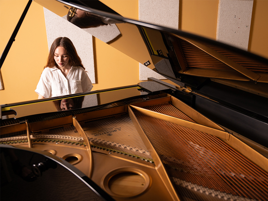 A College of Charleston female student playing a grand piano, captured from a low angle showing the piano's interior.