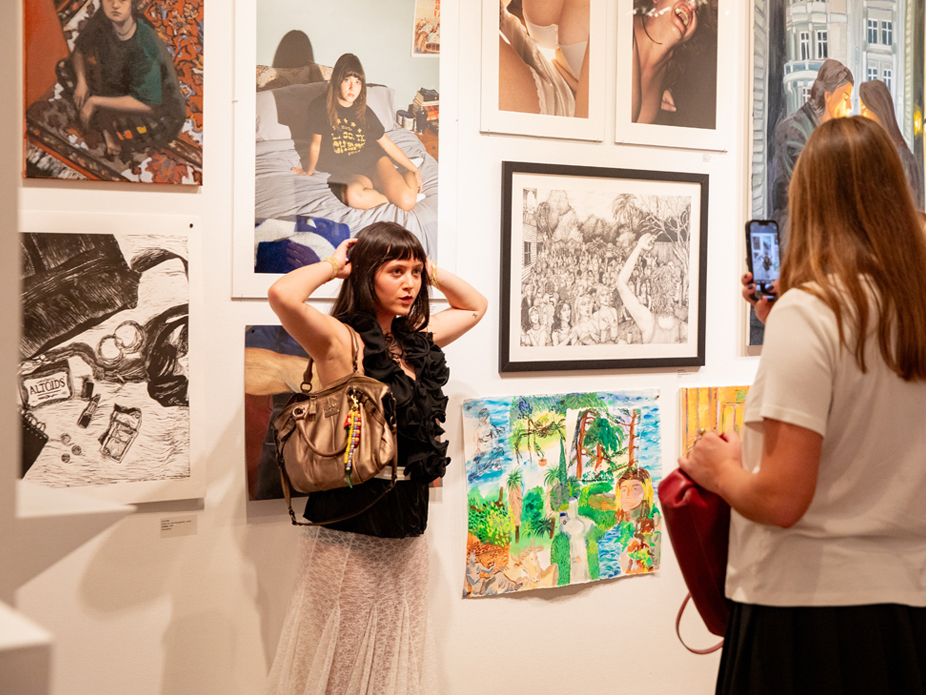 Visitors engaging with an artist and her artworks at an art exhibition.