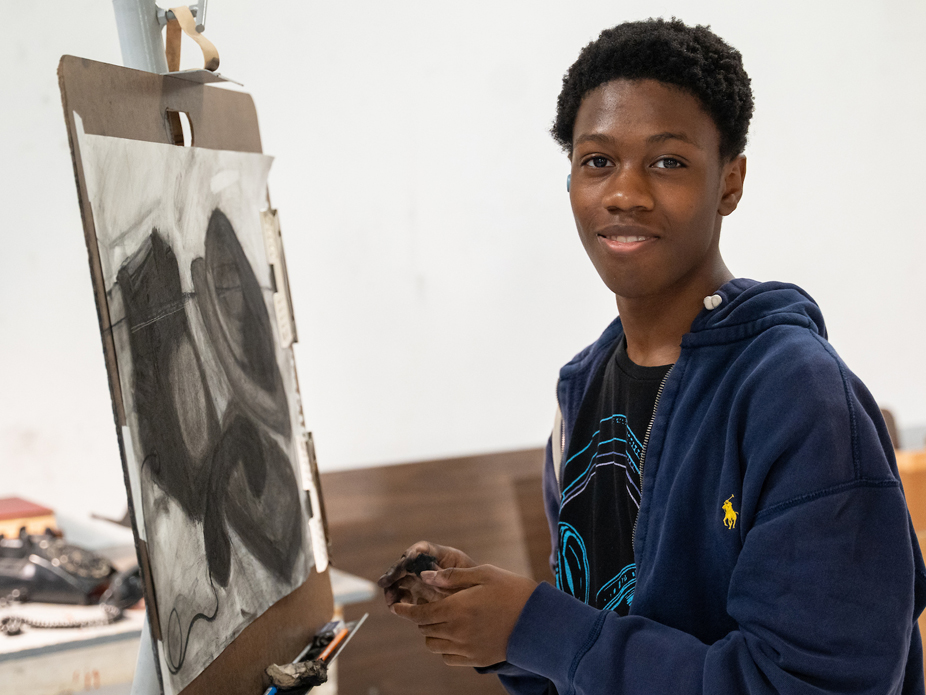 A student smiling while working on a charcoal drawing at an art studio.