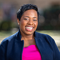 Professional portrait of Veronica Vereen, a smiling woman wearing a pink top and a navy jacket, set against a soft outdoor background.