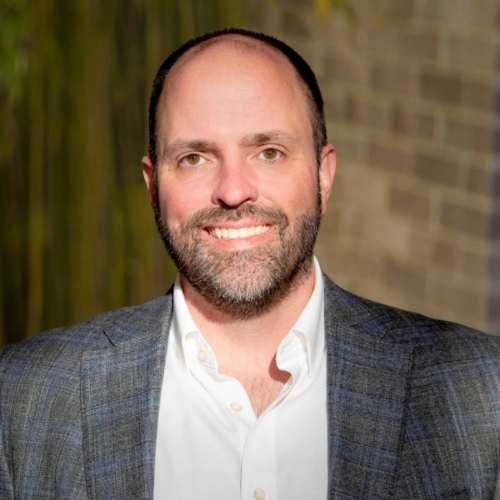A man smiling in front of a brick wall, or brickwall backdrop