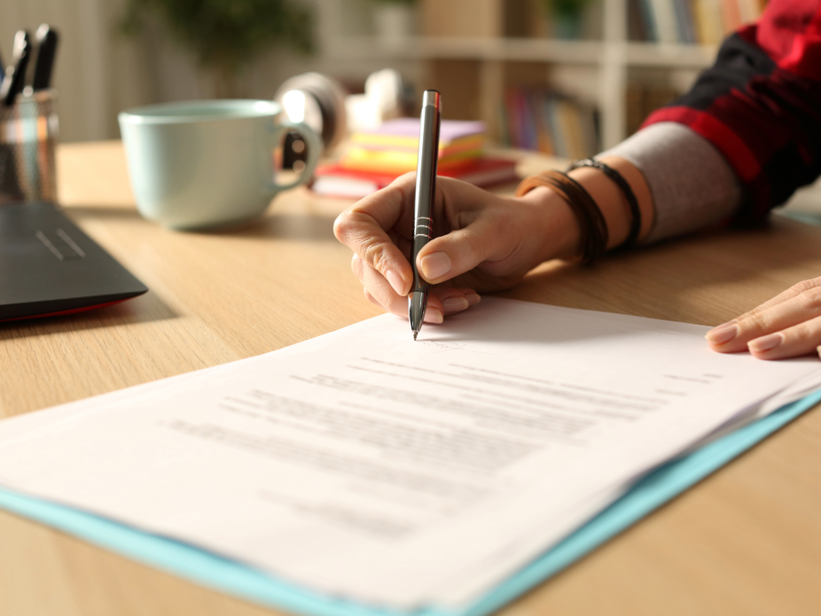 Close up of person writing with a pen on paper at desk