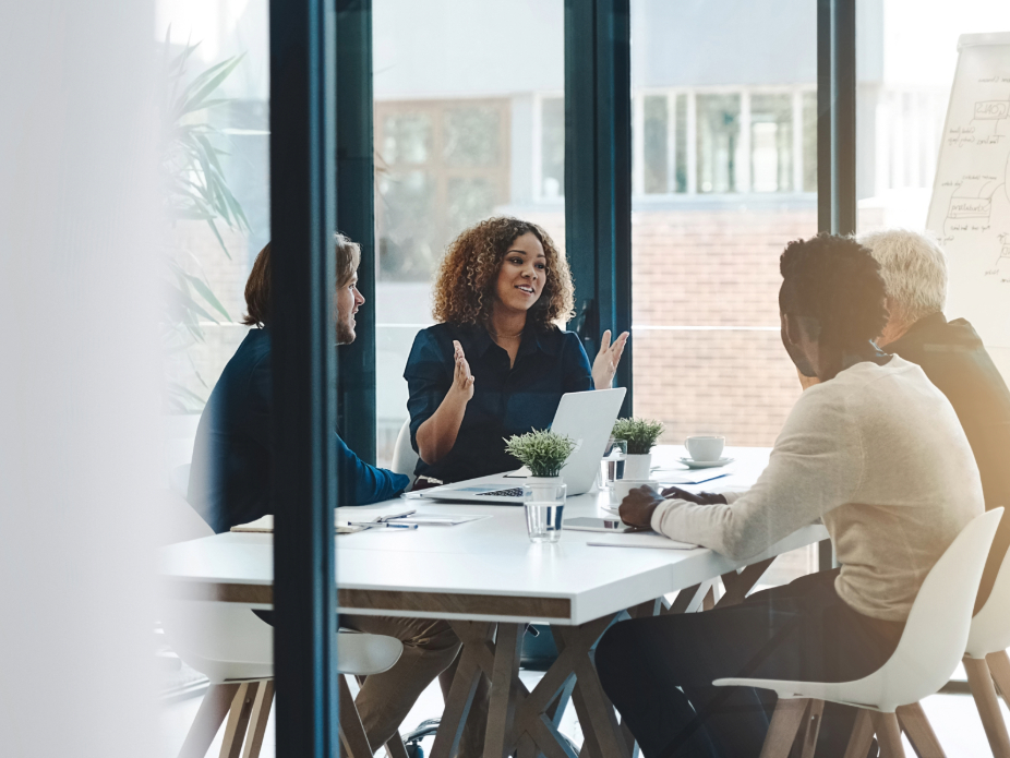 A group of professionals collaborating in a modern meeting room, with one person presenting ideas on a laptop.