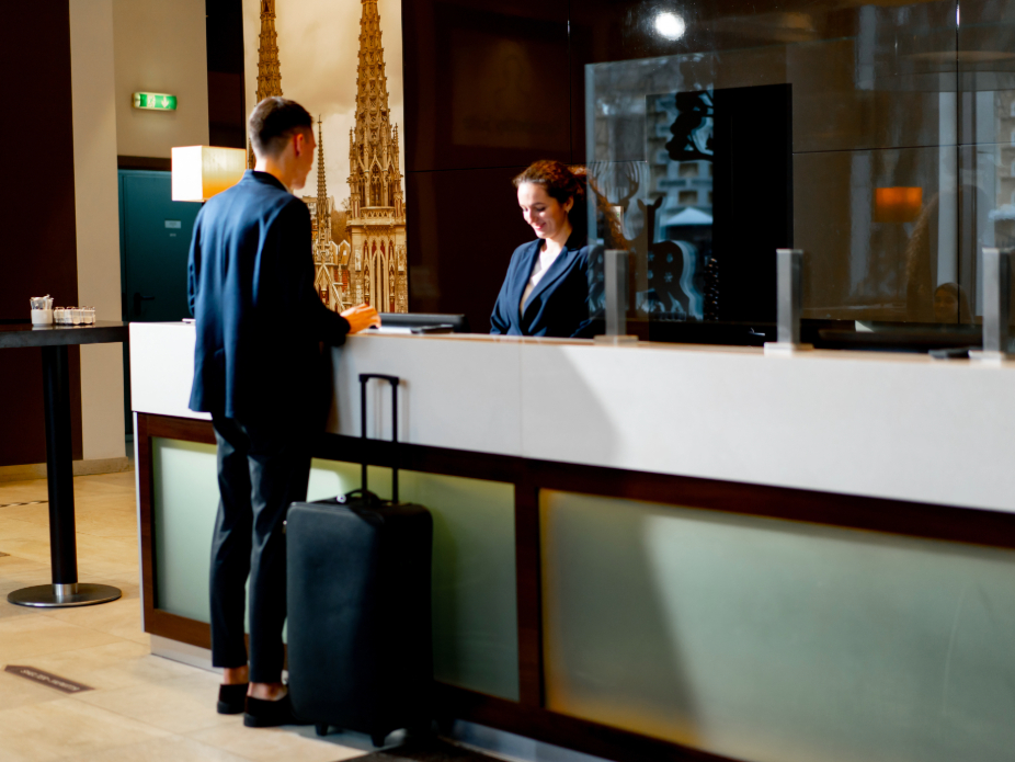 A woman behind a desk, checking a man with a suitcase into a hotel
