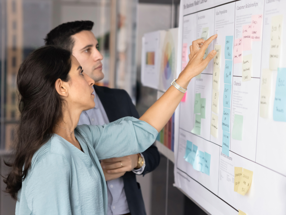 Two professionals collaborating in front of a board filled with sticky notes and diagrams.