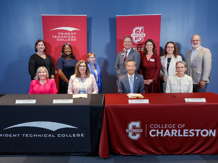 A group of people in professional attire smiling in front of banner with the Trident Tech and College of Charleston banners