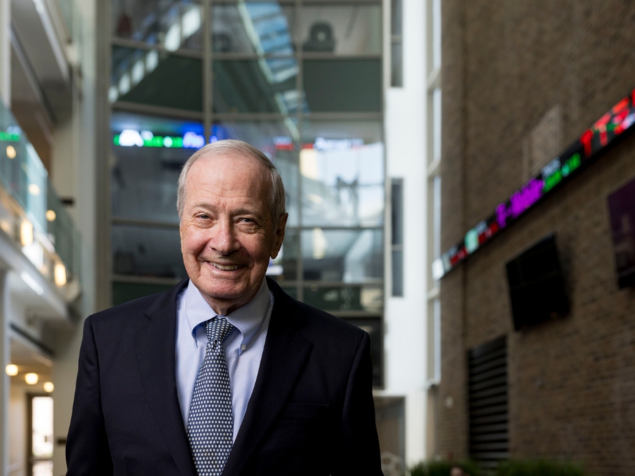Photo of man smiling in a business suit with stock ticker in the background