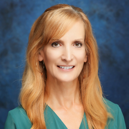 Professional headshot of a woman with long blonde hair, wearing a green blouse, set against a blue background.