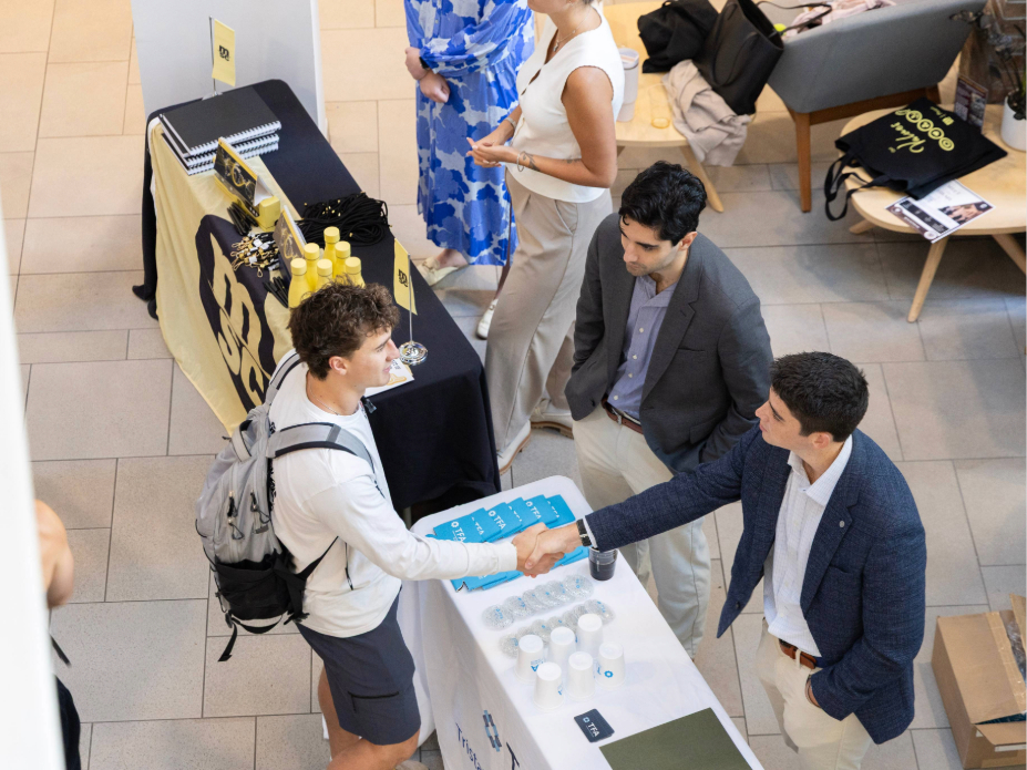 A student shaking hands across a career fair employer table
