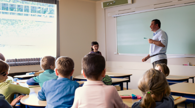 male teacher in front of younger students in classroom
