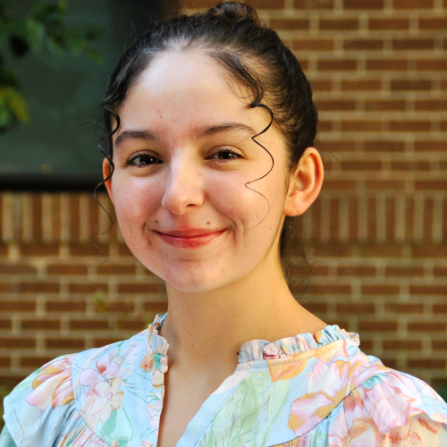Portrait of Adrianna Sowders smiling, with her hair pulled back, and wearing a light-colored floral shirt