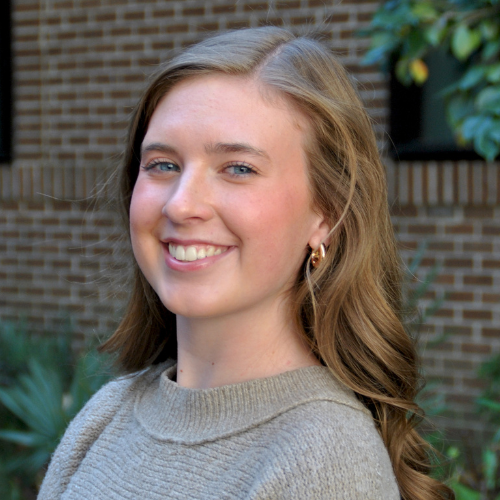 Headshot of Allie Johnson with blone hair, smiling in front of a brick building exterior.