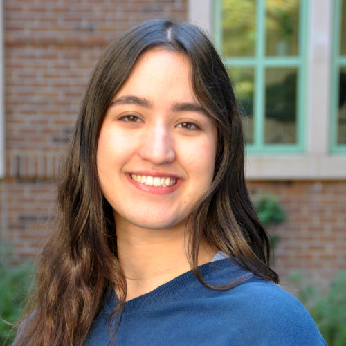 Headshot of Franny Fitch smiling and blue sweater in front of a brick background.