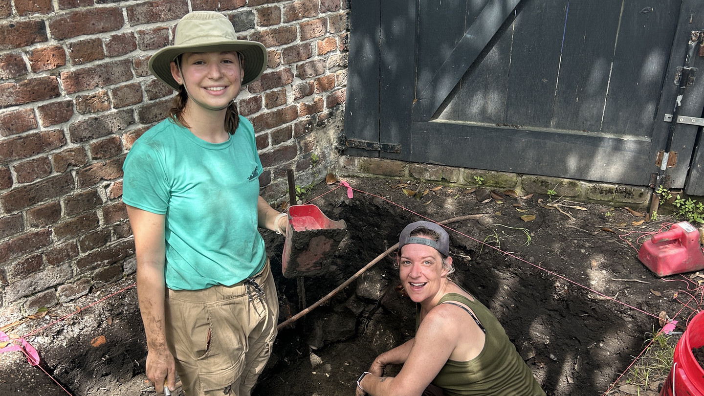 Two female students in the middle of doing a dig during field work.