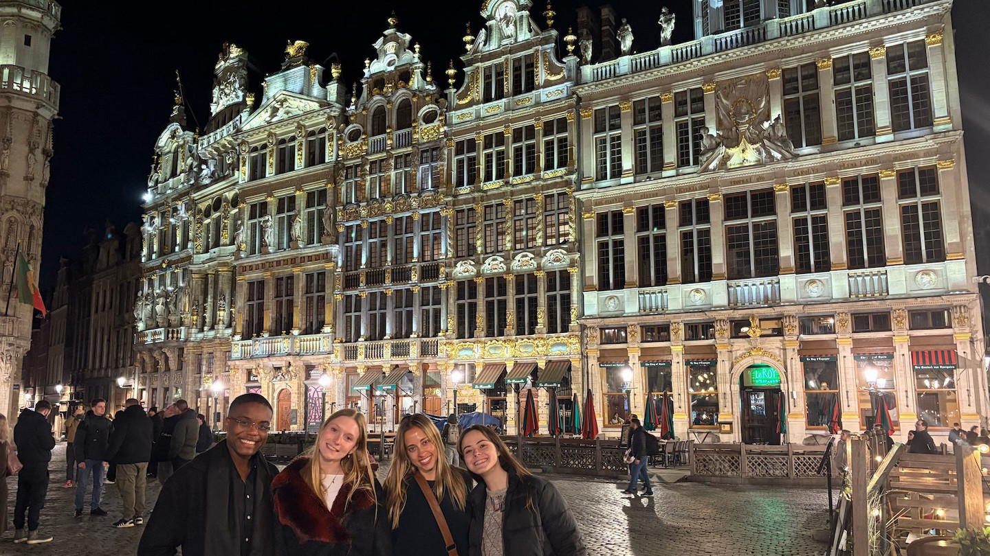 Four students standing in front of a beautiful, large building in Belgium.