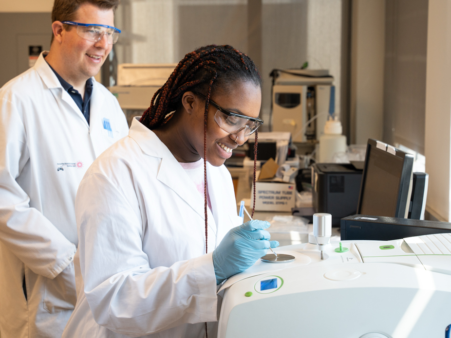 A scientist in a lab coat and safety glasses is using a precision instrument to conduct chemistry experiments.