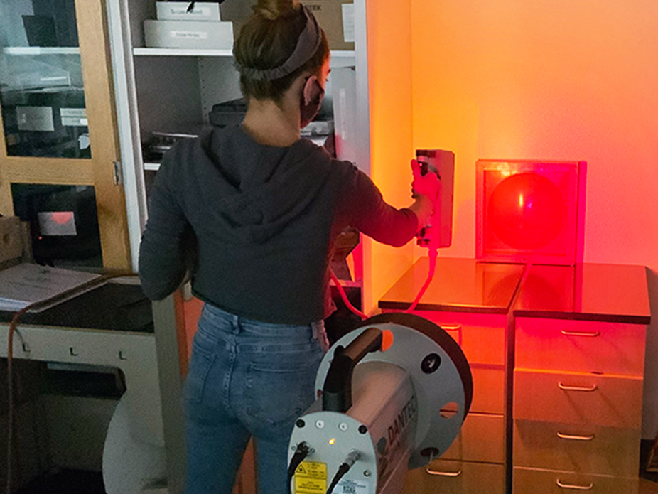 A student using laser optics to perform an experiment in a dimly lit room, illuminated by red light.