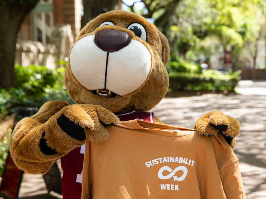 Cheerful mascot Clyde the Cougar proudly holds up a shirt that promotes "SUSTAINABILITY WEEK."