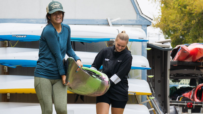 Two College of Charleston students carrying a kayak between them.