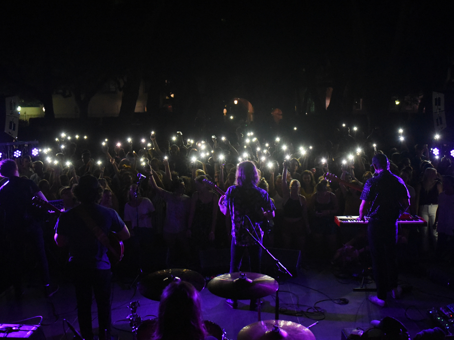 A view from behind a band performing in concert at the Cistern Yard shows appreciative fans holding up their cell phones.