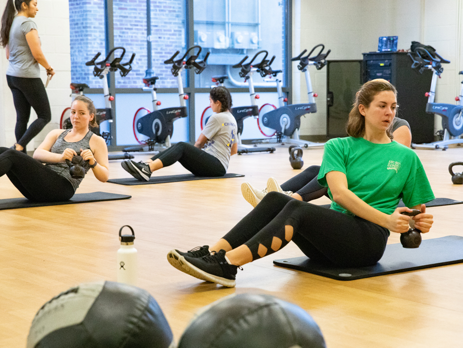 College of Charleston women work out with kettle weights on mats in a fitness class.