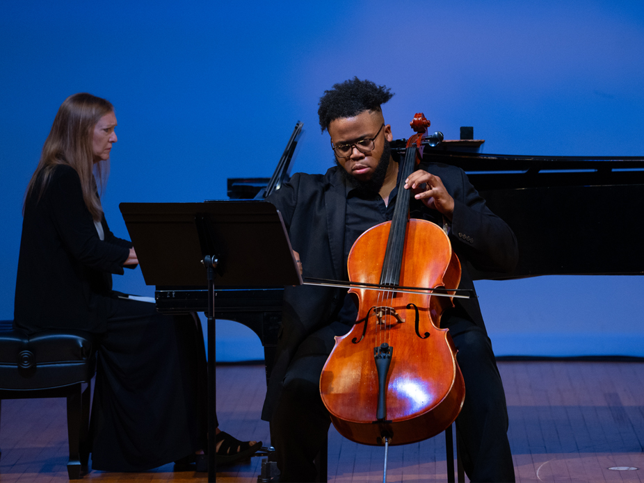A College of Charleston male student performs on the cello with a woman accompanying on the piano.