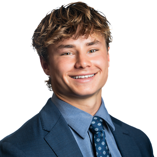 A professional headshot of Evan Camrie smiling, wearing a suit and tie against a white background.