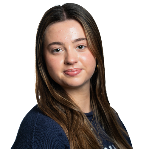 Headshot of Katie Kaminski, a young woman with long brown hair poses for a professional headshot, wearing a dark sweater and a subtle smile.