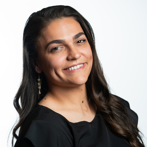 Portrait of Kait Mounce smiling with long dark hair wearing a black top and earrings.