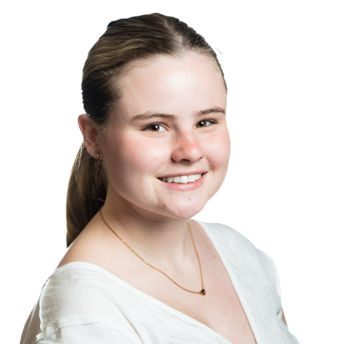Smiling portrait of MK Wilshire, a young woman with long hair, wearing a white top and a delicate necklace.