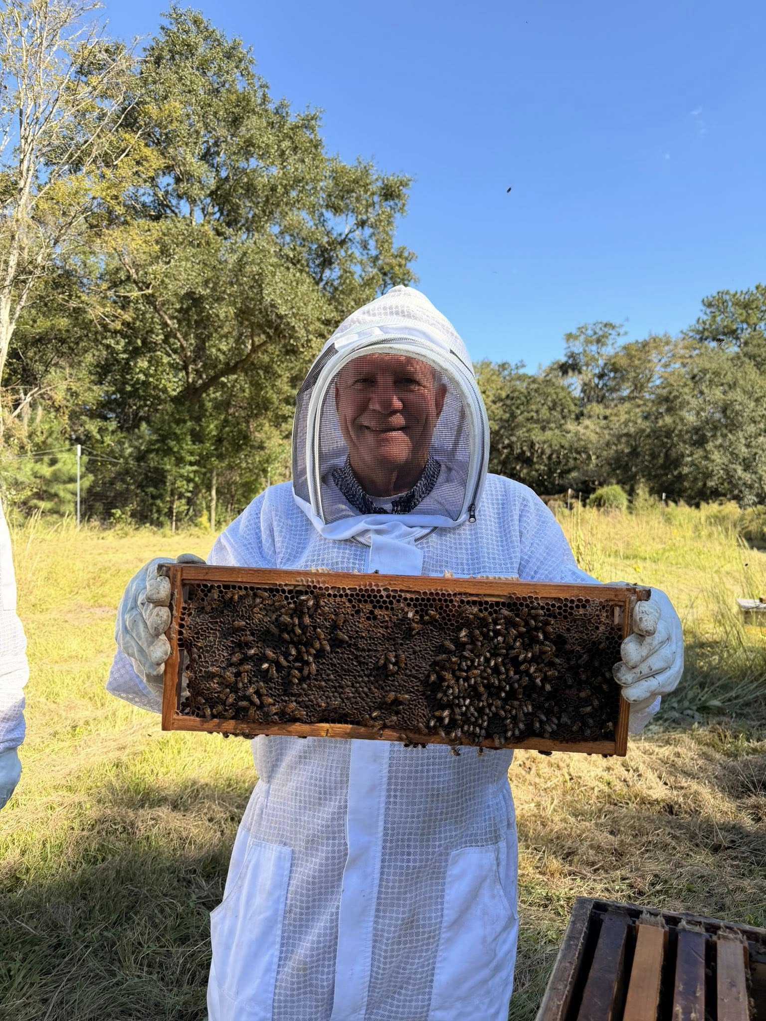 A member of the CofC Board of Trustees wears beekeeper equipment as he holds up a hive of bees.