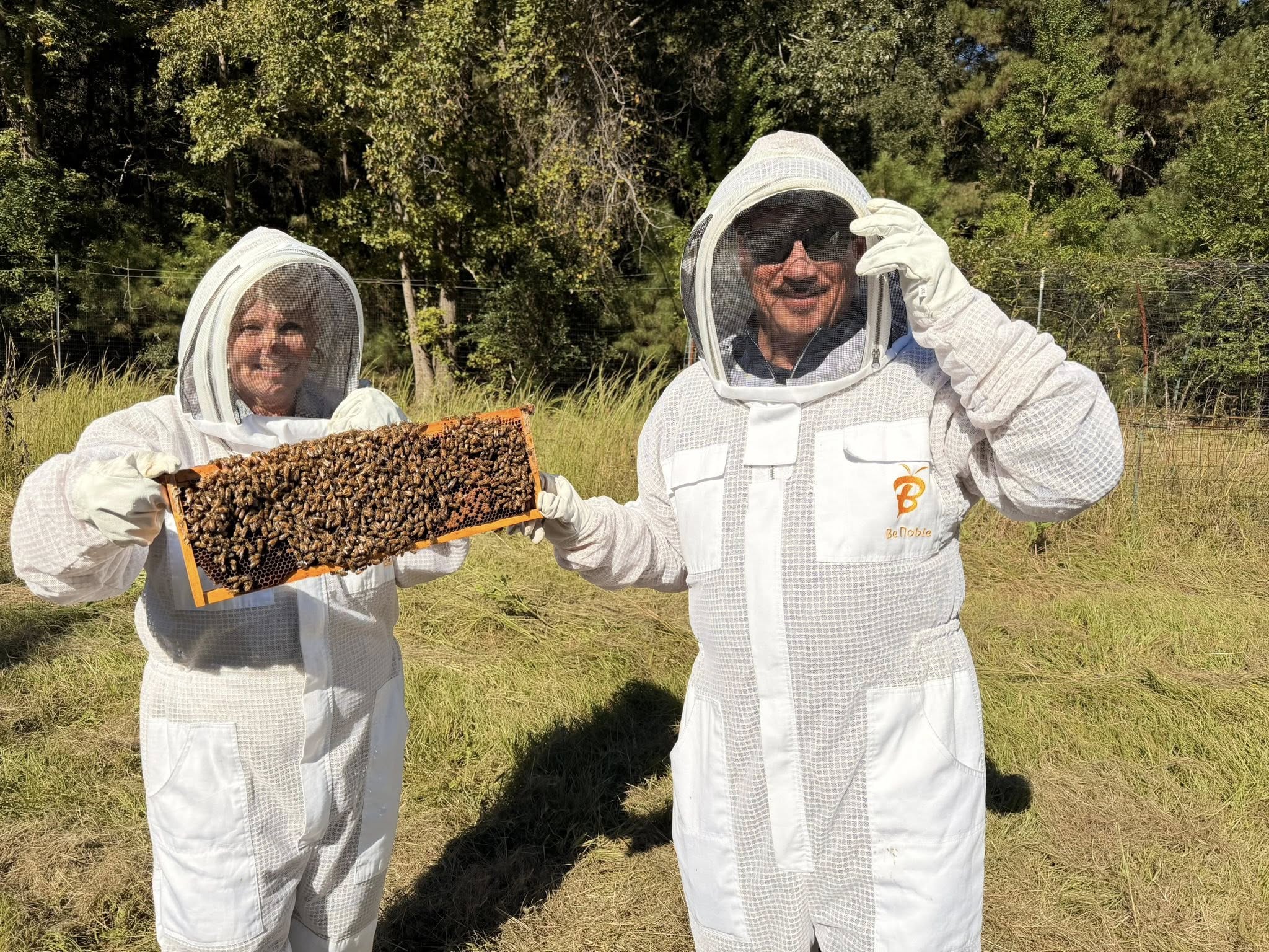 A woman in beekeeper protective equipment holds up a hive of bees.